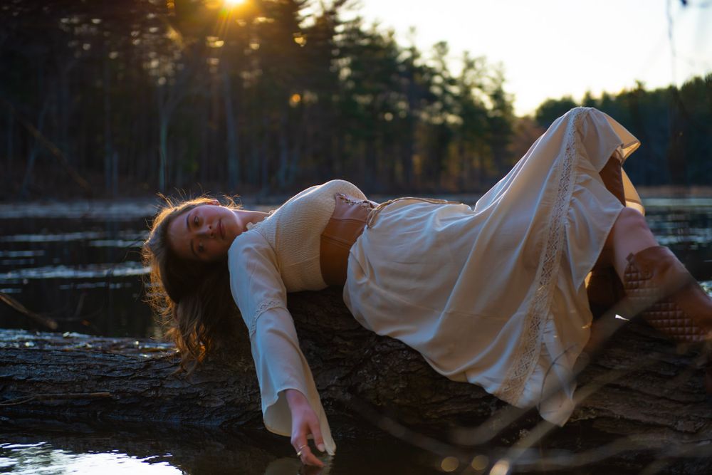 A dramatic pose on driftwood shows a figure in white against golden sunset light reflecting on water.