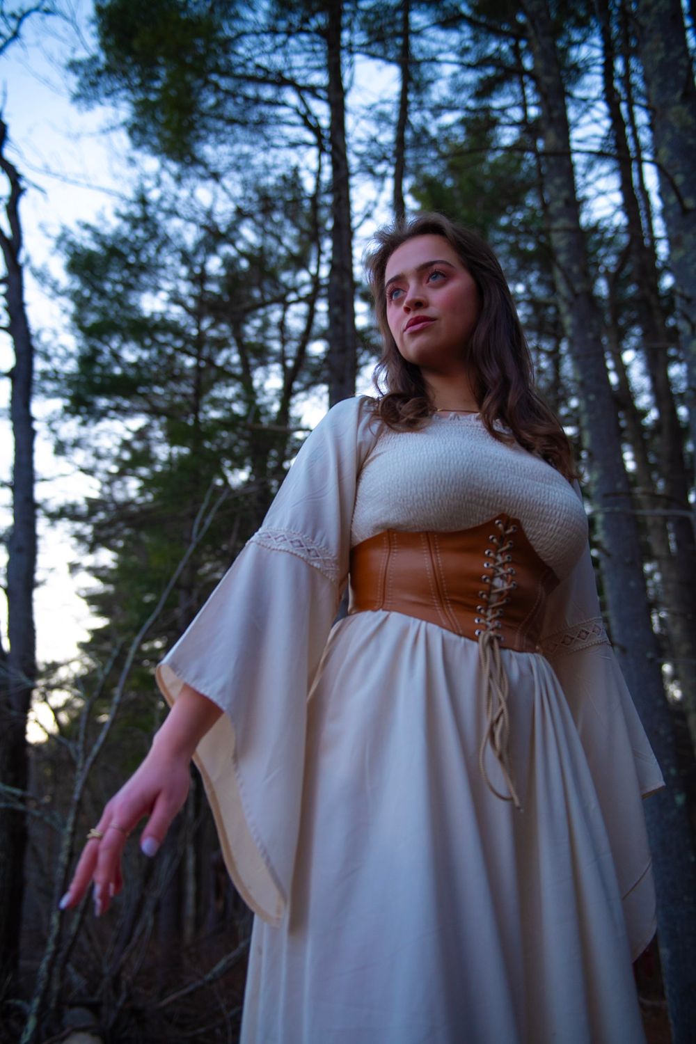 Medieval-inspired white dress with corset photographed in moody forest setting.