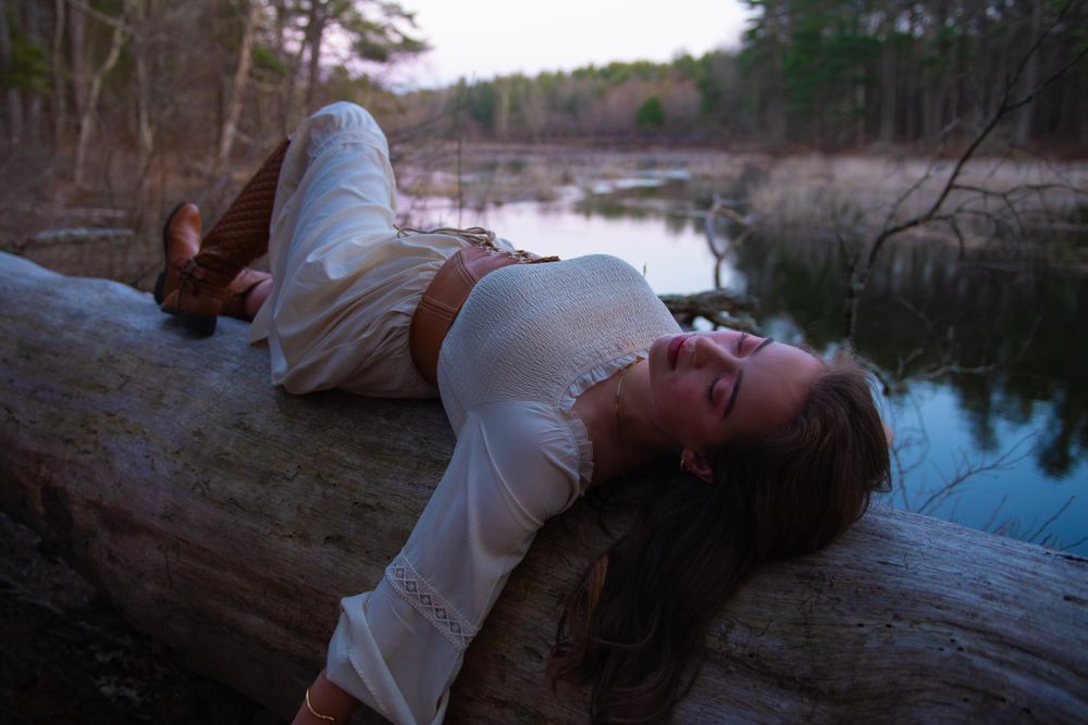 Dreamy forest photoshoot featuring white dress and fallen log over water.
