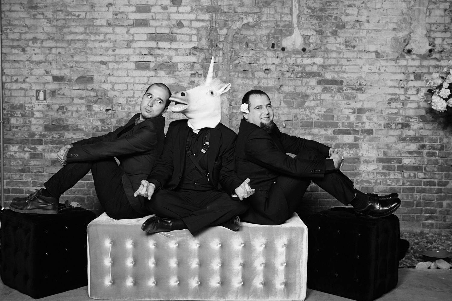 Black and white photo of three performers in suits with one wearing a unicorn mask.