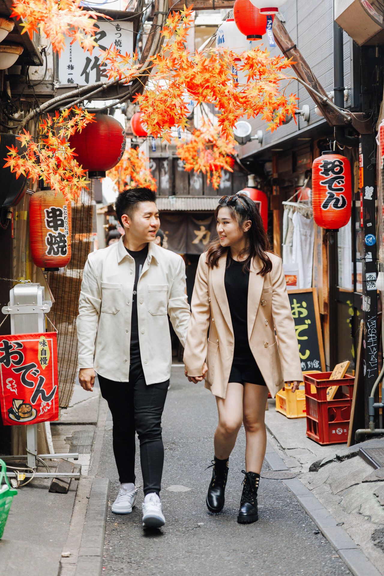 A couple walking hand in hand through a Japanese alley with red lanterns and autumn foliage.