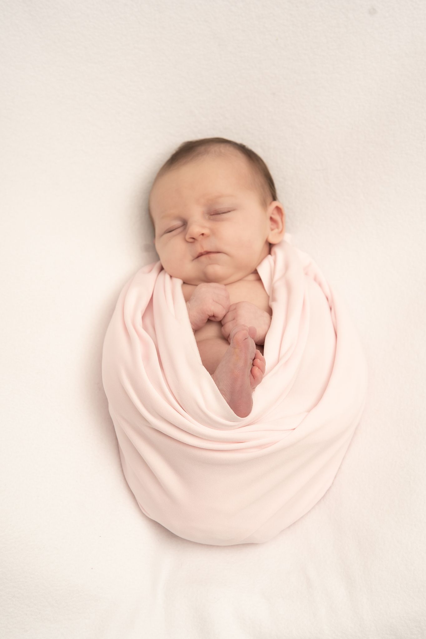 Sleeping newborn baby swaddled in soft pink wrap against white background.