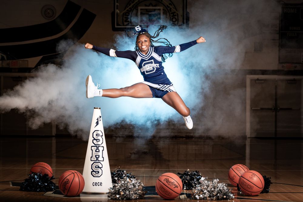 Senior girl cheerleader jumps in the air. Blue smoke surrounds her.