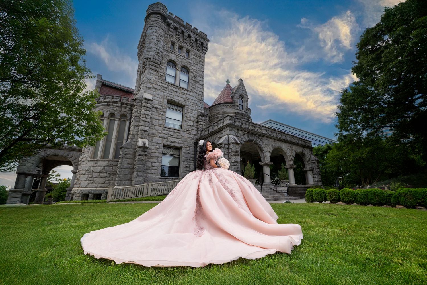 Flowing pink dress contrasts against gothic stone castle architecture at sunset.