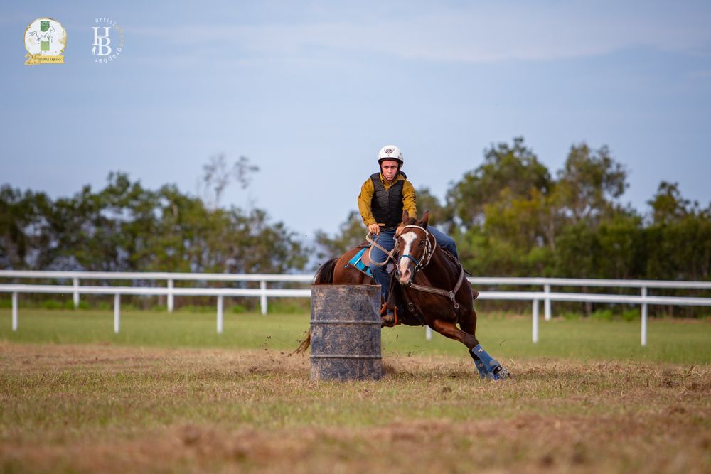 Barrel racing competitor on horseback navigates around a barrel on a dusty arena track during competition.