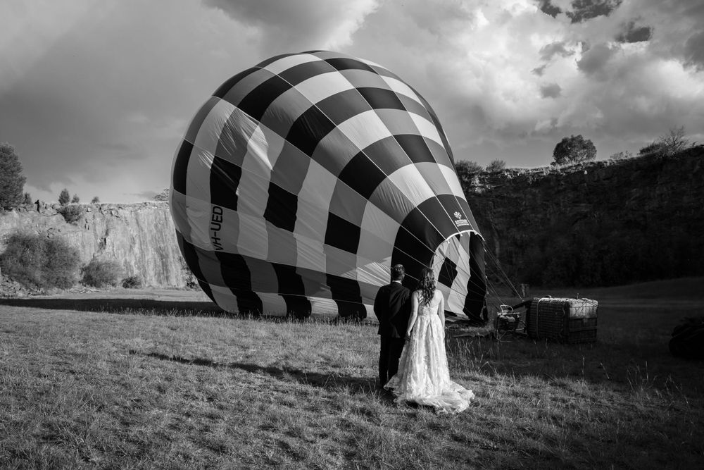 Wedding couple standing near a black and white checkered hot air balloon in a dramatic black and white photo.