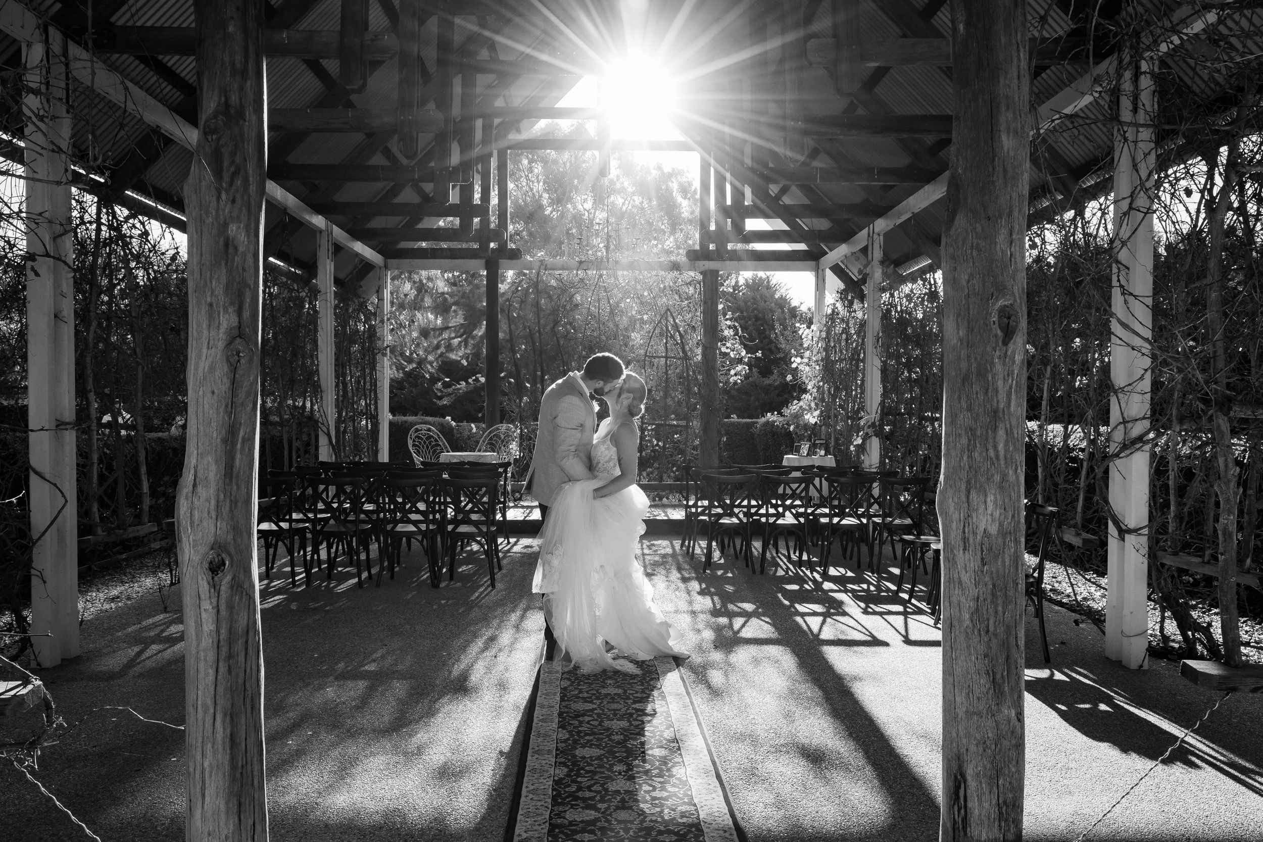 Black and white photo of couple dancing in rustic venue with dramatic lighting.