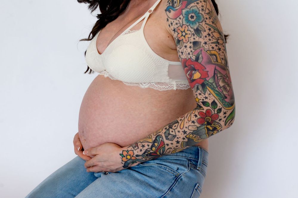Side view photo progression showing pregnant woman's growing belly in jeans and colorful tattoo sleeve over white background.
