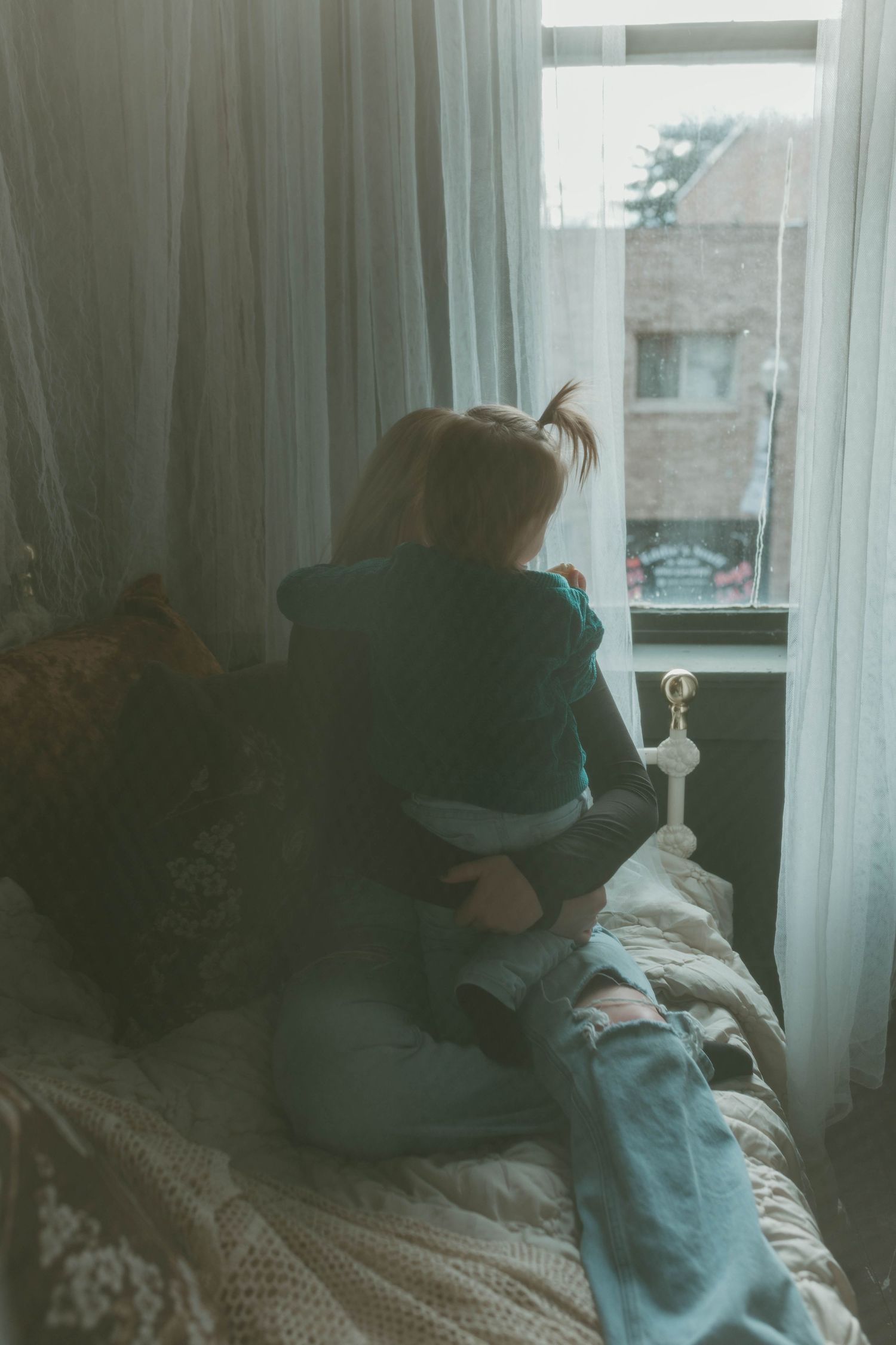 A silhouette sits by a window with soft light filtering through sheer curtains.
