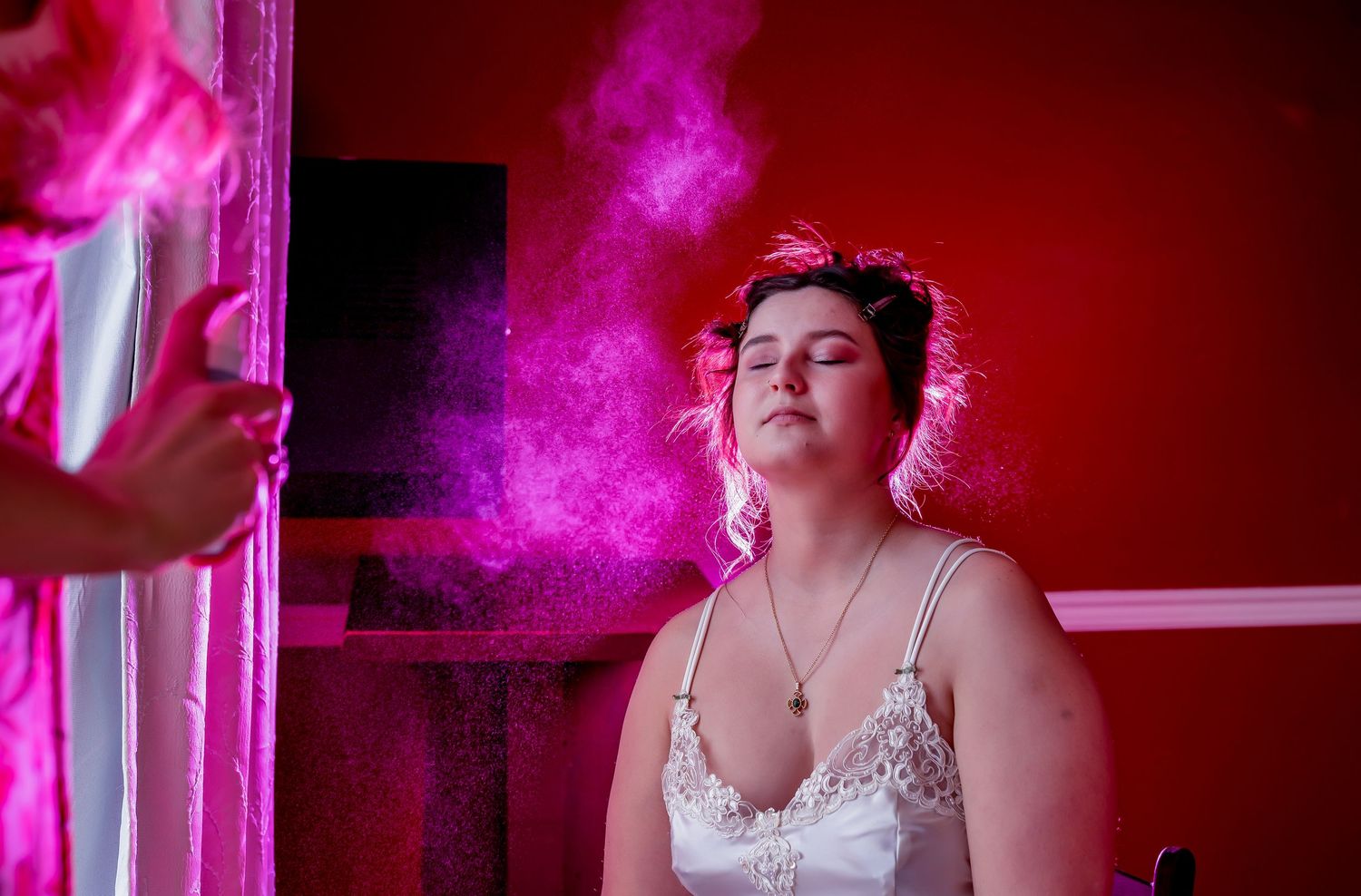 A person in a white lace top illuminated by dramatic pink smoke against a red background.