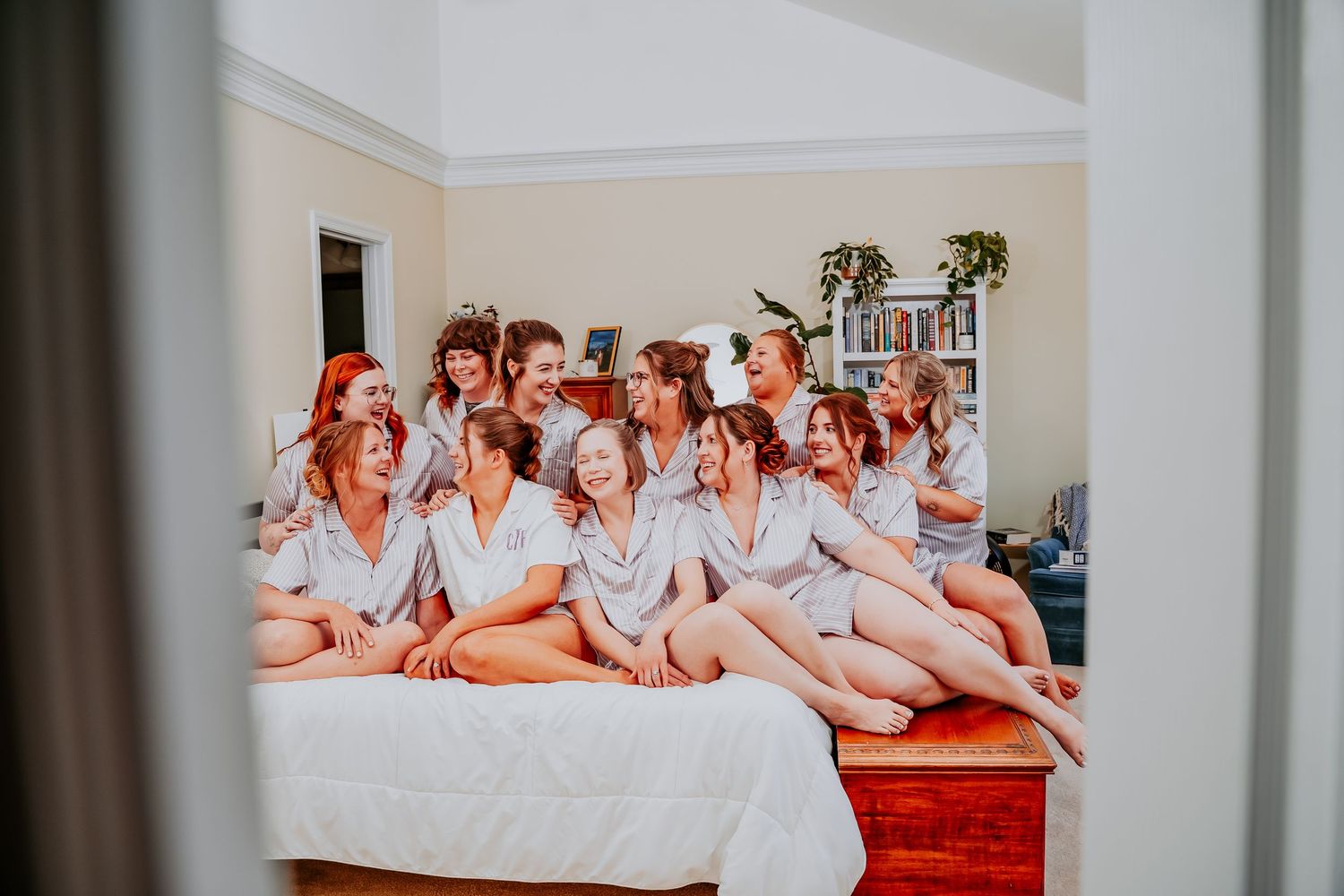 Four photos show a group of women in white robes lounging on a bed during a bridal party preparation.