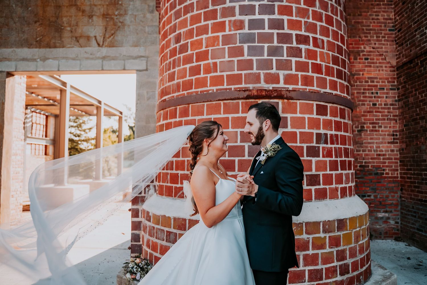 A couple shares a romantic moment in front of a rustic brick building during a wedding photo session.