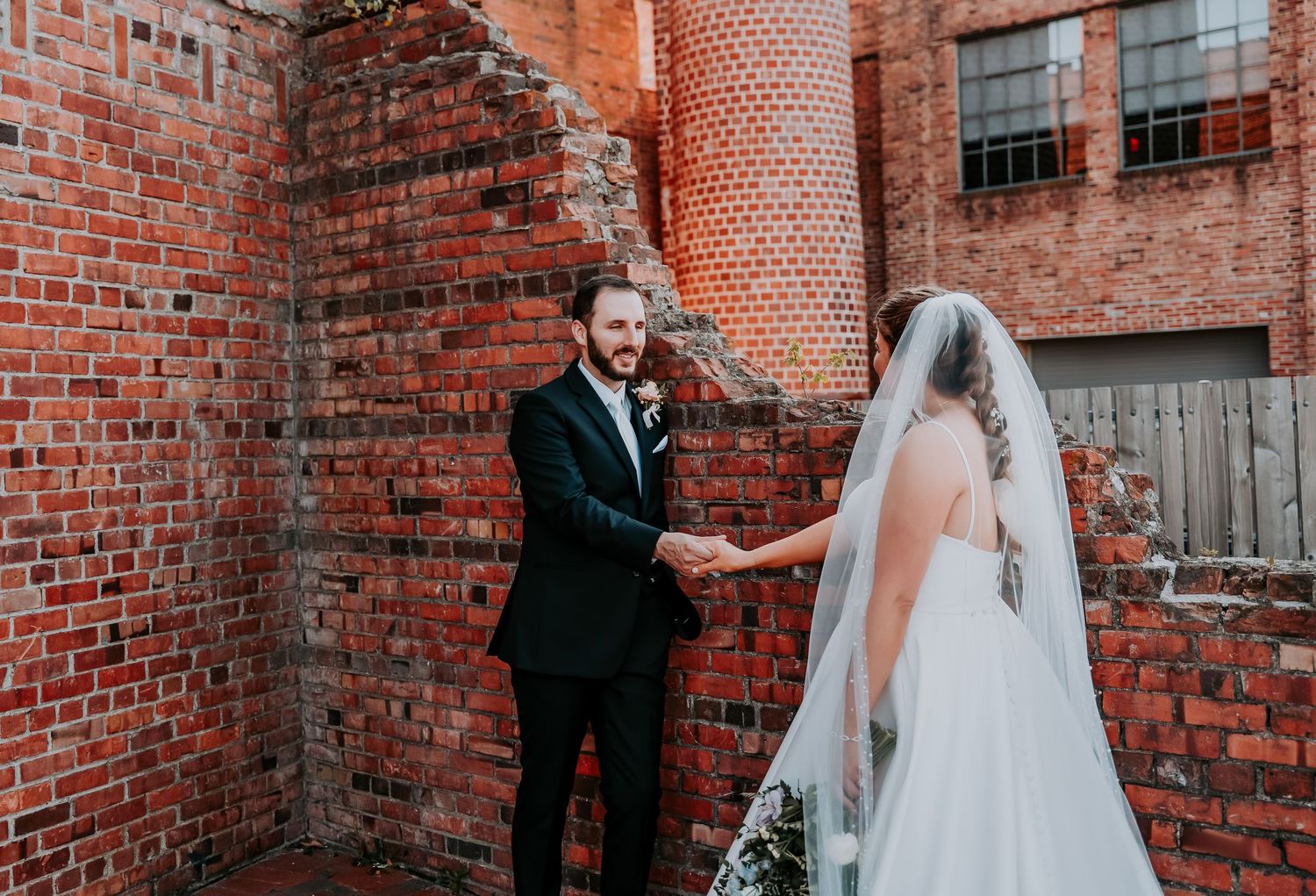 Wedding couple shares romantic moments against rustic brick wall backdrop during outdoor portrait session.