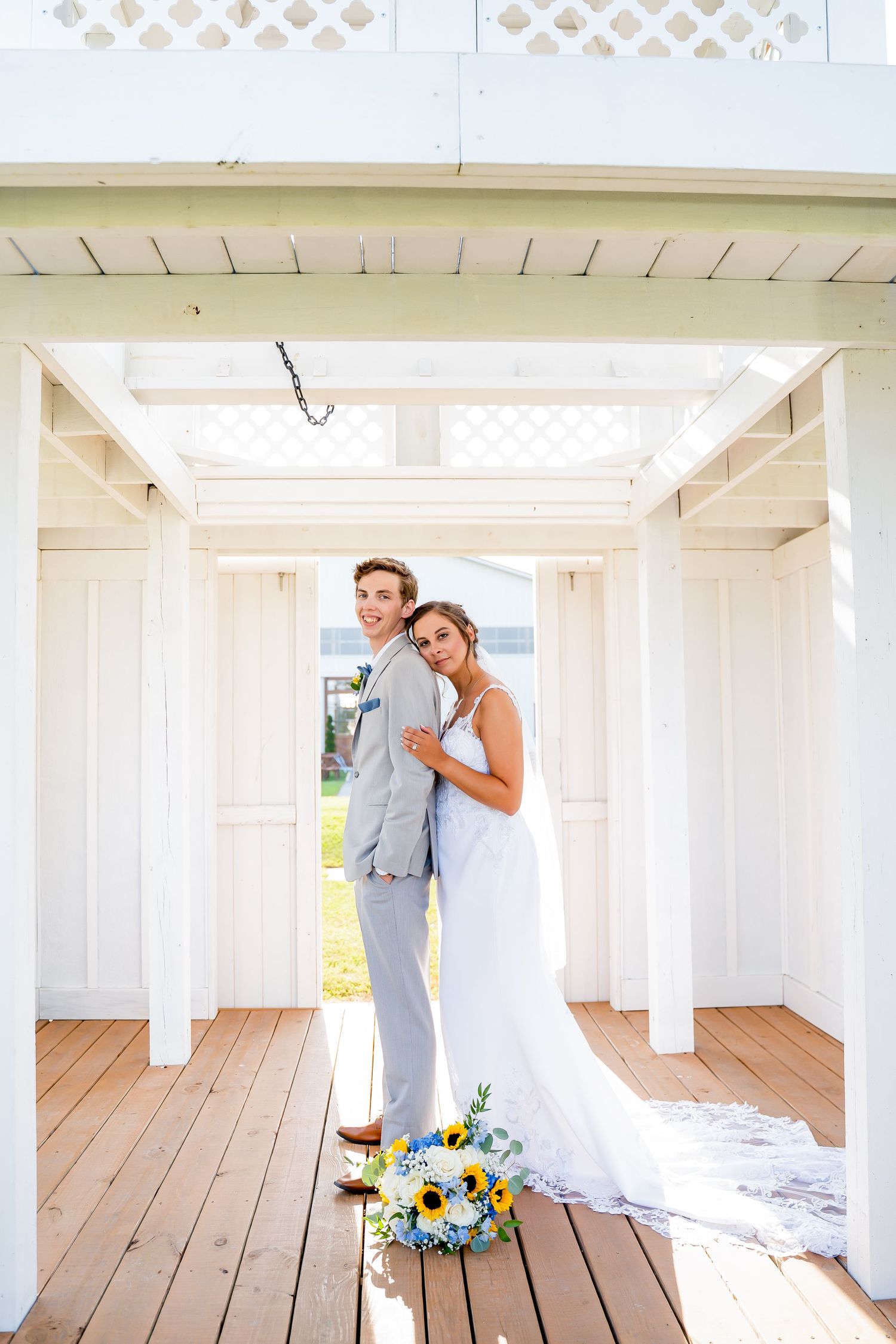 A romantic wedding couple embraces in a white covered porch area with wooden floors and beams.