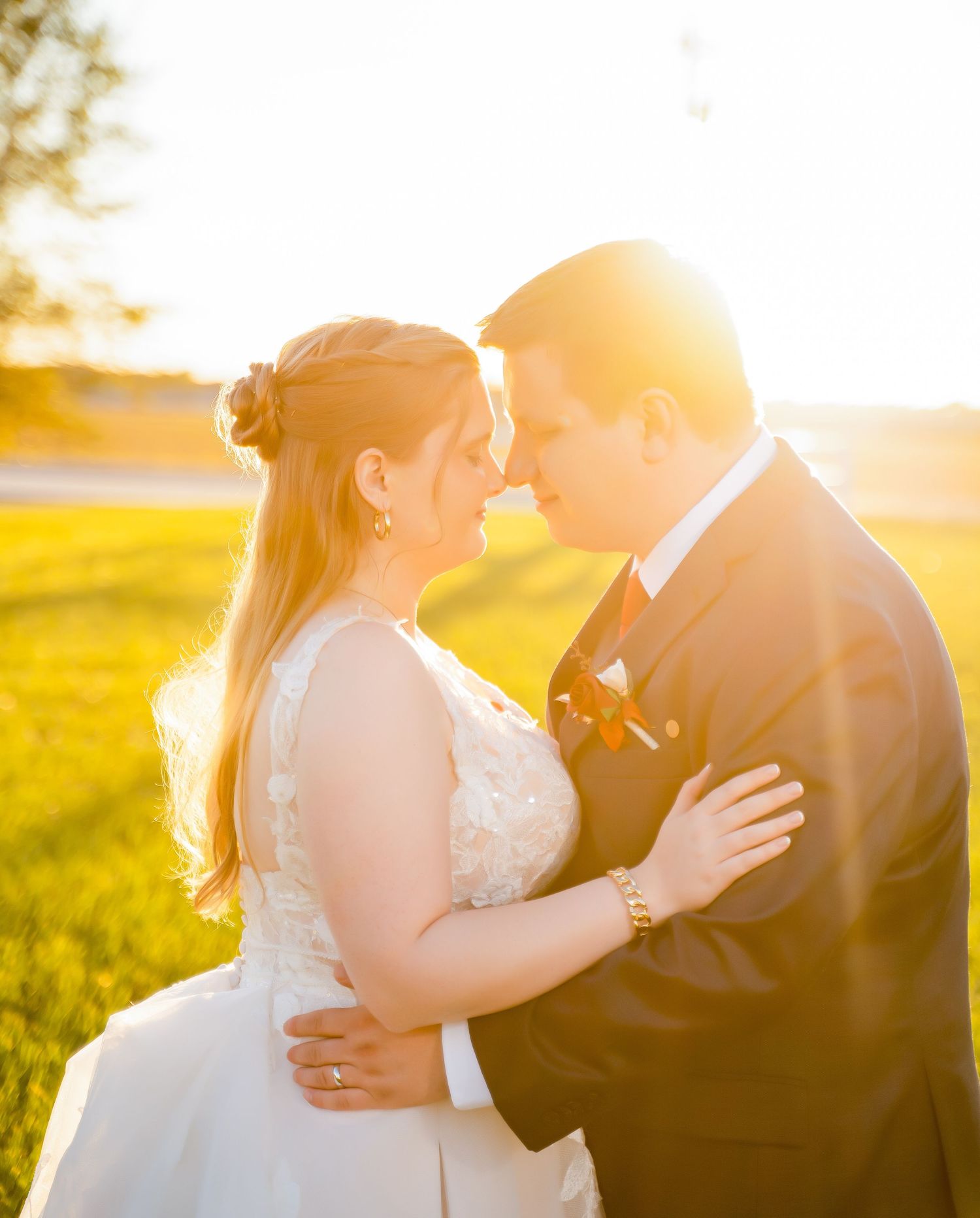 A romantic wedding couple shares a tender kiss during golden hour in a sunlit meadow.