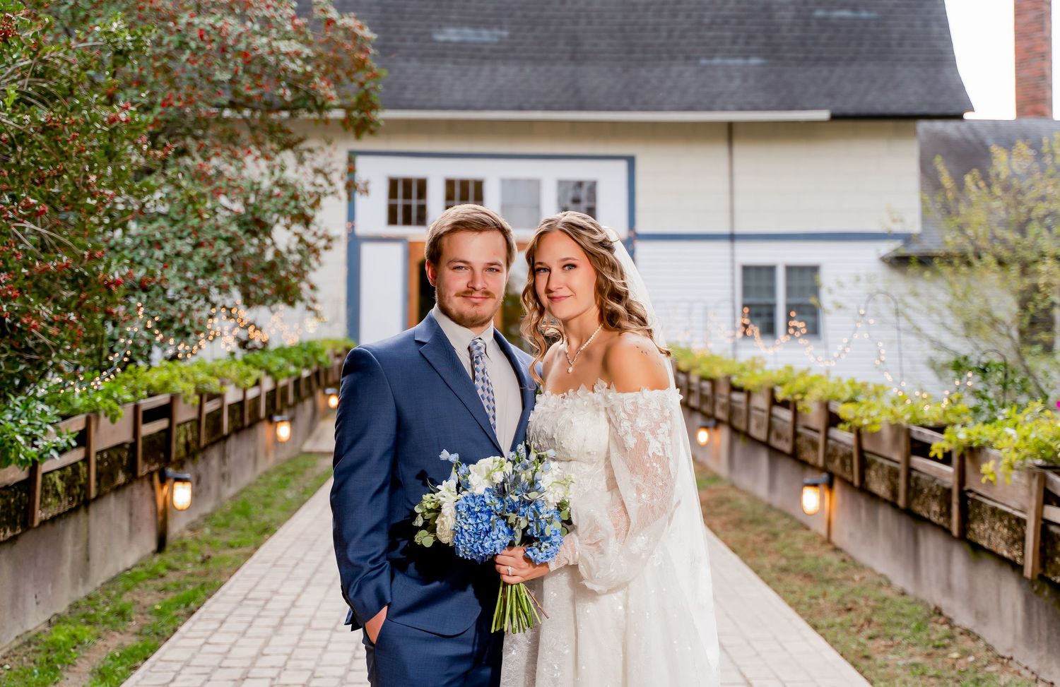 A romantic wedding couple poses for photos on a rustic wooden bridge surrounded by lush greenery and spring blooms.
