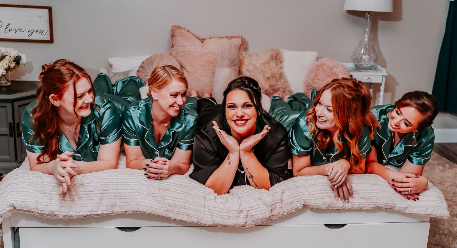 A group in matching green floral robes lying together on a white bed with pink pillows.