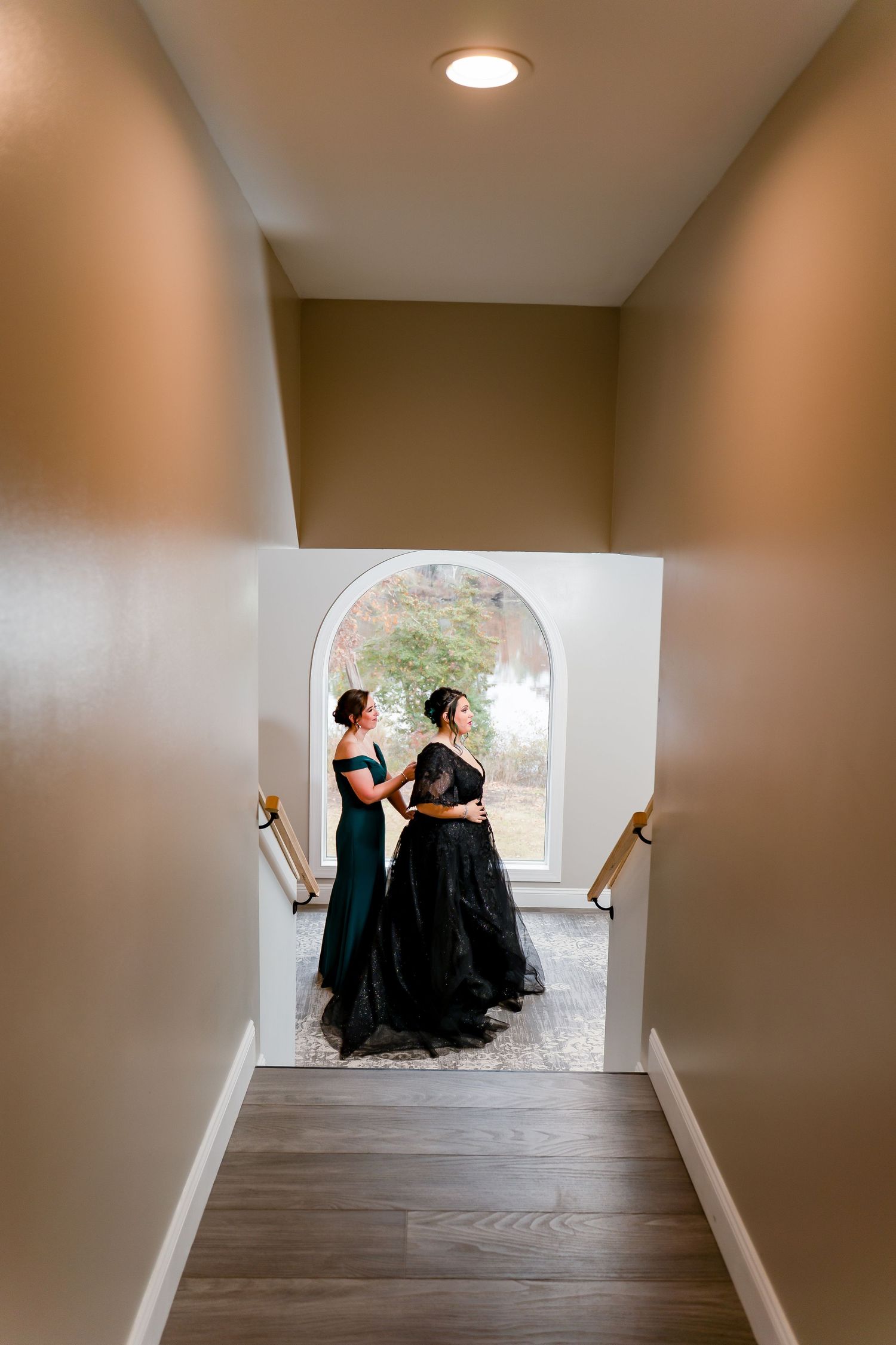 Two figures in black dresses stand in a minimalist hallway with recessed lighting and hardwood floors.