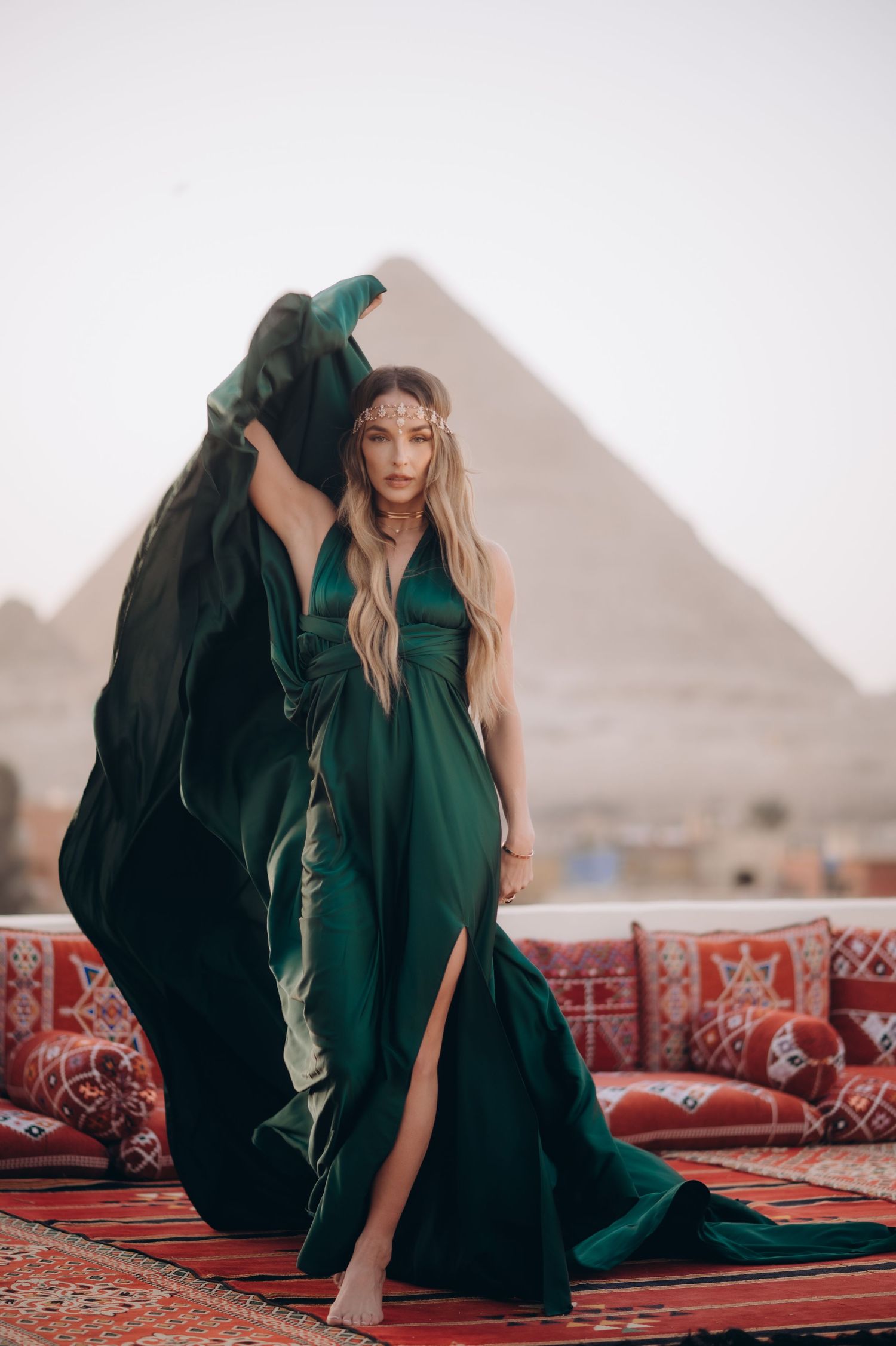 Woman in flowing black abaya poses gracefully on traditional carpets with Egyptian pyramids in background.