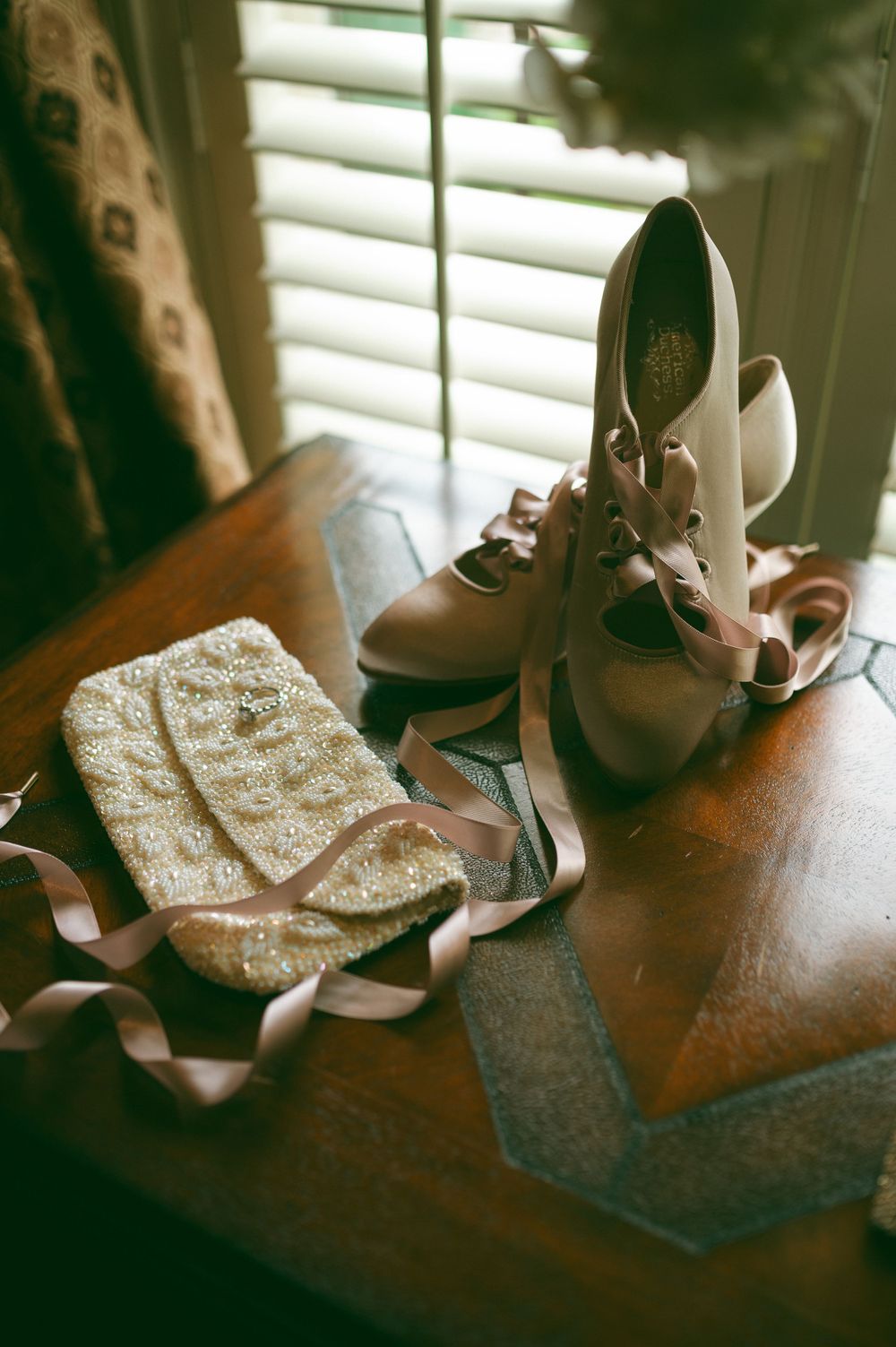 Wedding accessories including bridal shoes and a beaded clutch on a wooden surface.