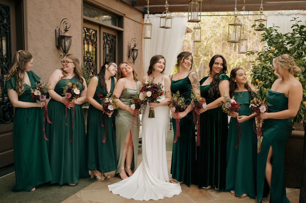 Bridesmaids in emerald green dresses stand with bride at an elegant indoor venue.