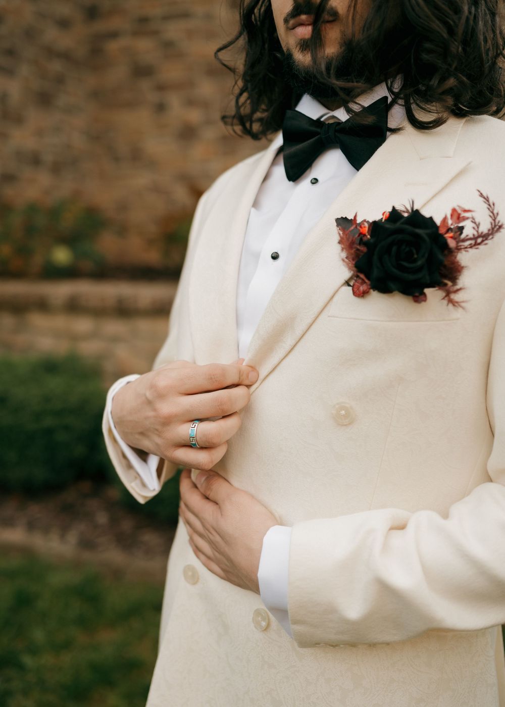 Detail shot of a cream tuxedo with black bowtie and dark burgundy boutonniere.