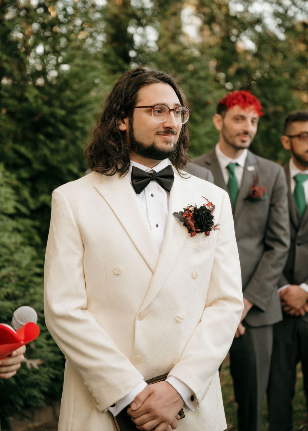 Wedding party members in white and grey suits standing outdoors with autumn foliage in background.
