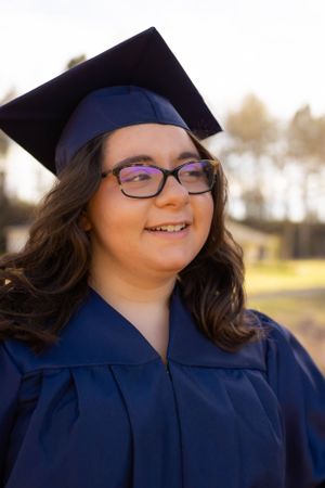 Graduate wearing blue cap and gown smiles during outdoor photo session.
