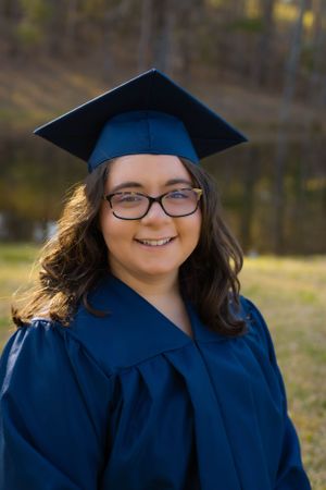 Graduate in traditional blue cap and gown smiles during outdoor ceremony photos.