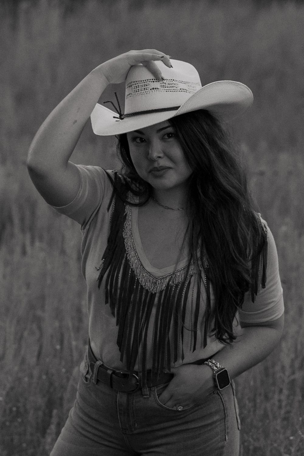 Black-and-white portrait of a woman holding her cowboy hat on her head with one hand in her pocket during a creative session in Fort Worth.