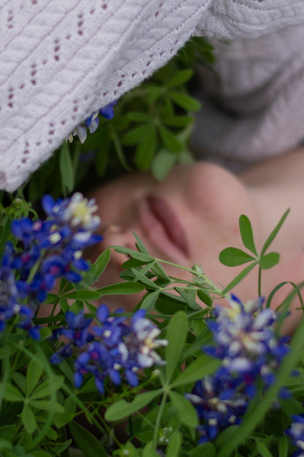 Close-up of bluebonnets partly covering a woman's face as she lays in a flower field during a creative portrait session in Benbrook, Texas.