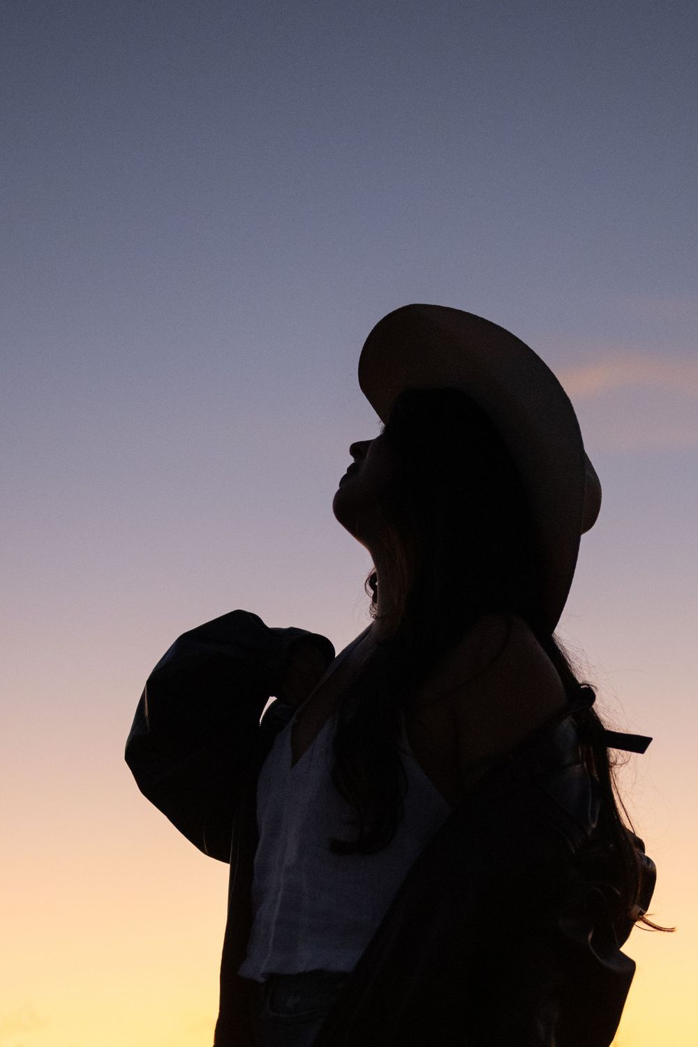 Silhouette of a cowgirl as dusk in Fort Worth during a creative portrait shoot, her head up, one hand adjusting jacket.