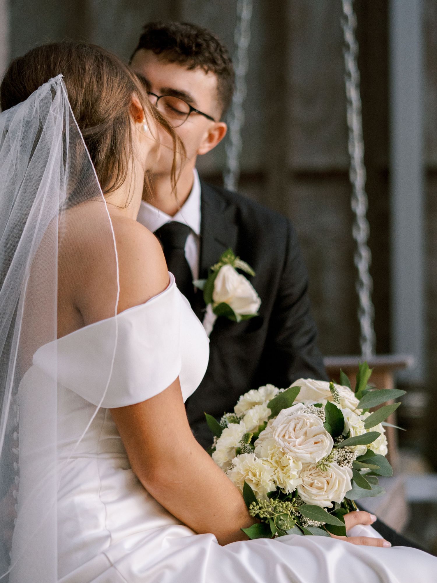 A romantic wedding moment captured with a white bridal bouquet of roses and greenery in a soft, intimate setting.