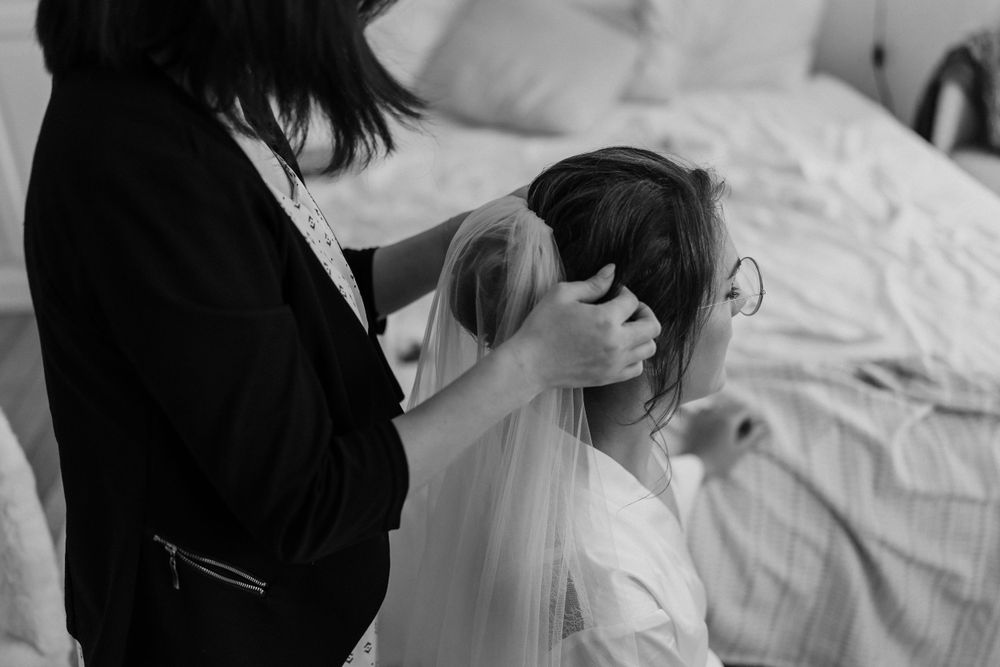 Black and white photo showing veil being placed during bridal preparation.