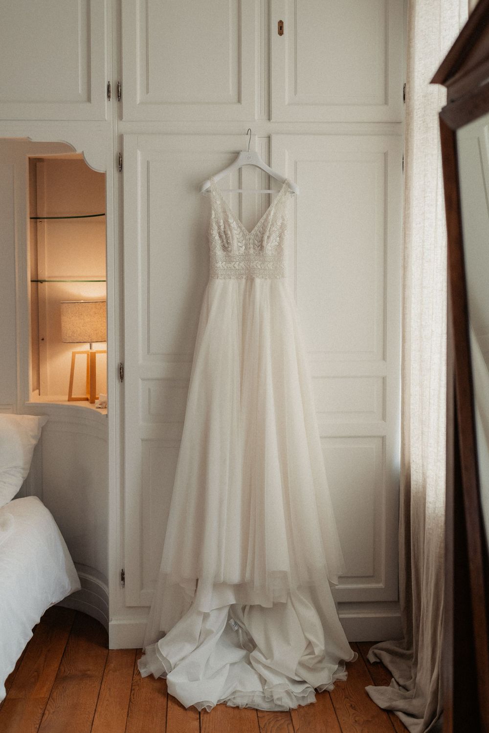 Beautiful white wedding gown hanging on wardrobe door in natural light.