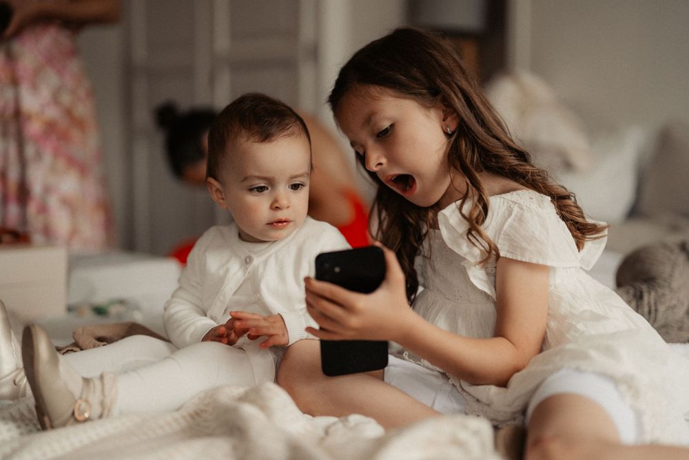 Two people in white outfits looking at a mobile device on a bed.