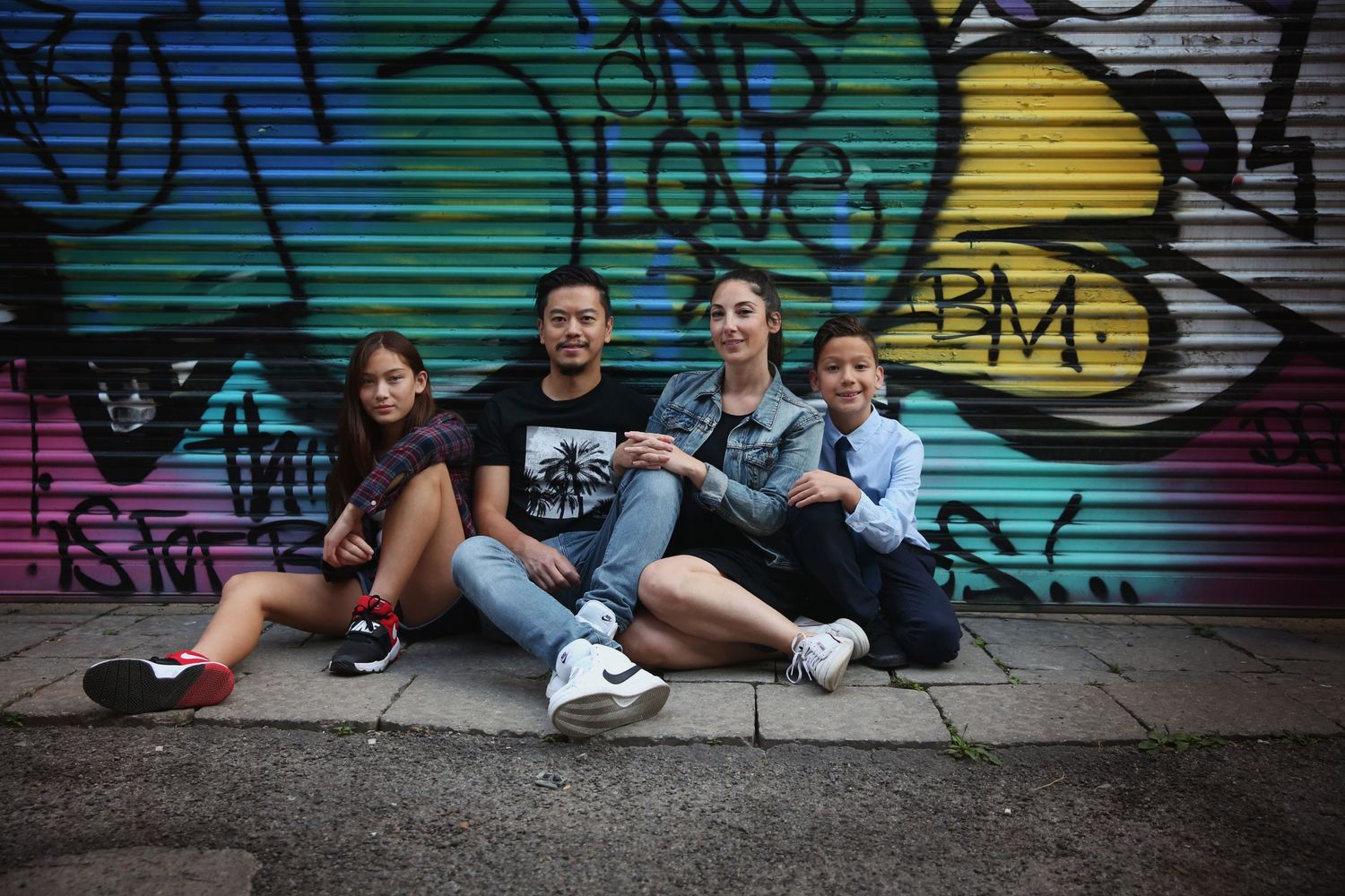 Group sitting against colorful graffiti wall in urban setting.