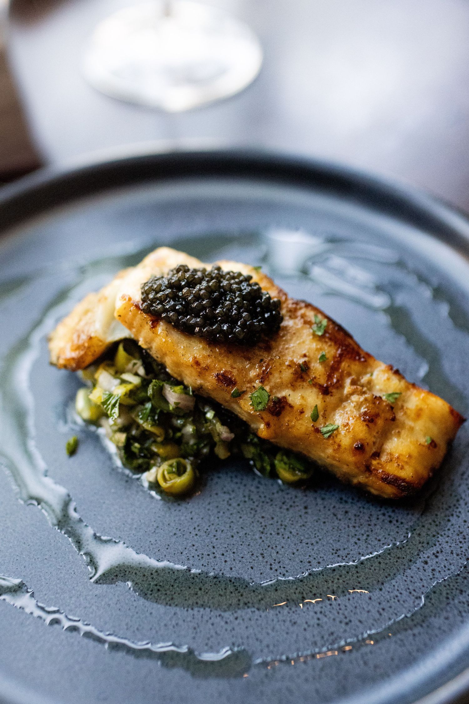 Pan-seared salmon fillet topped with black caviar served on a bed of sautéed greens on a dark plate.