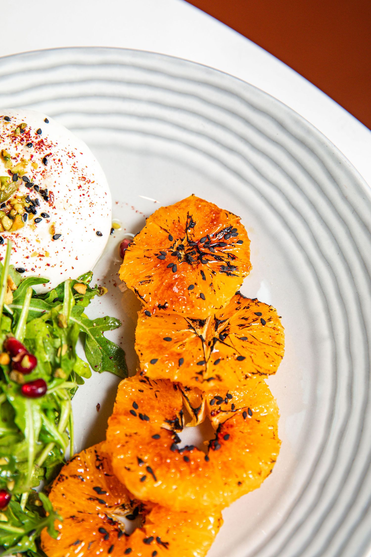 Fresh citrus salad with grilled orange slices and microgreens on a white textured plate.