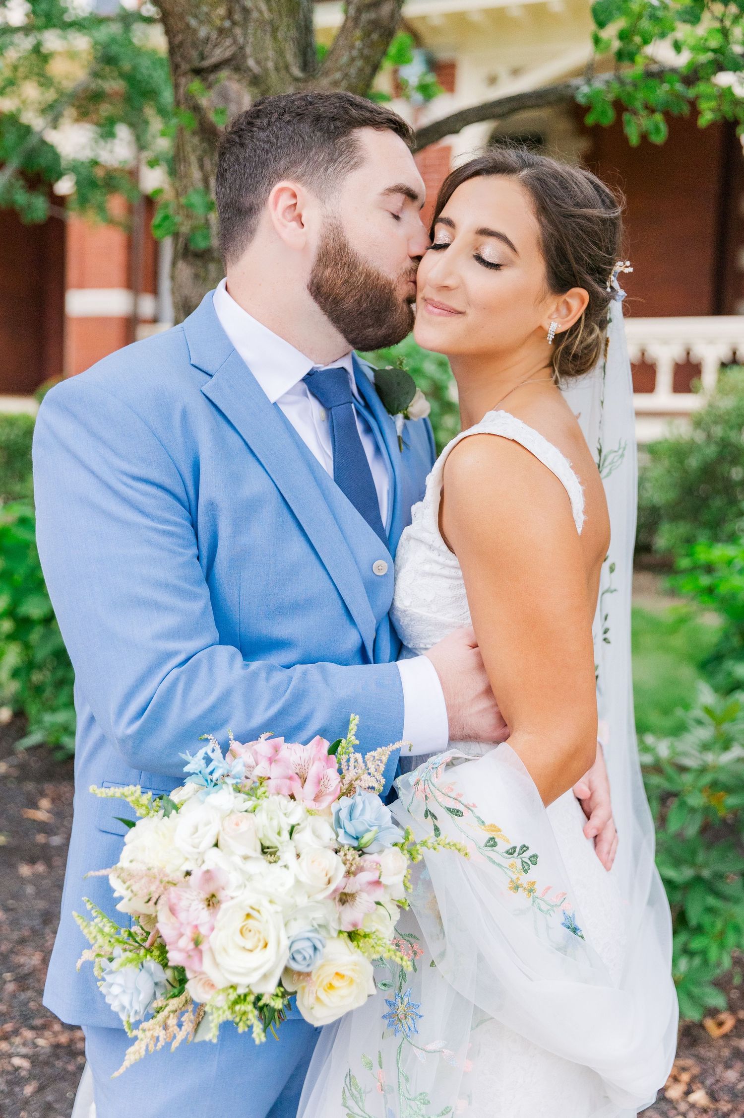 Beautiful spring wedding bouquet with pastel flowers against powder blue suit.