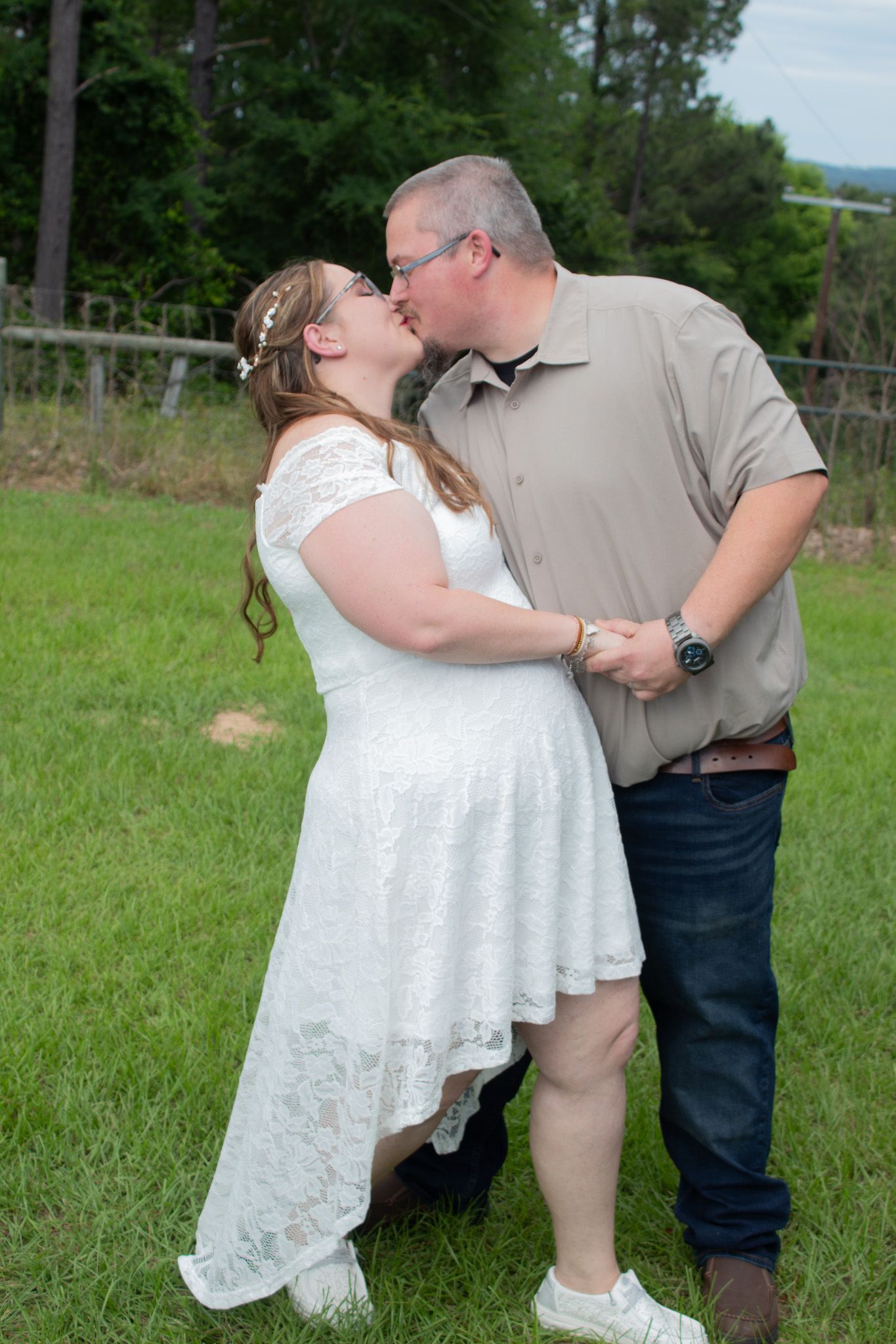 A romantic couple in wedding attire shares a tender kiss in a green field during their outdoor photo session.