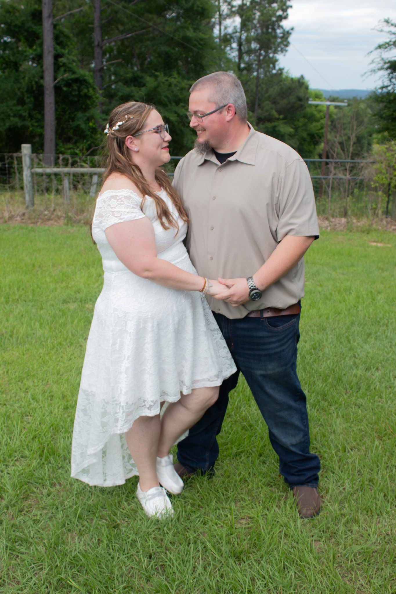 A couple dances together in a grassy field wearing white and beige casual attire.