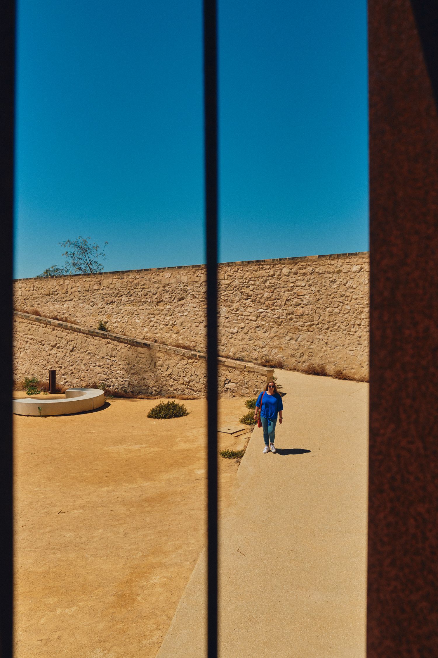 View through window frame of sandy courtyard with stone walls.