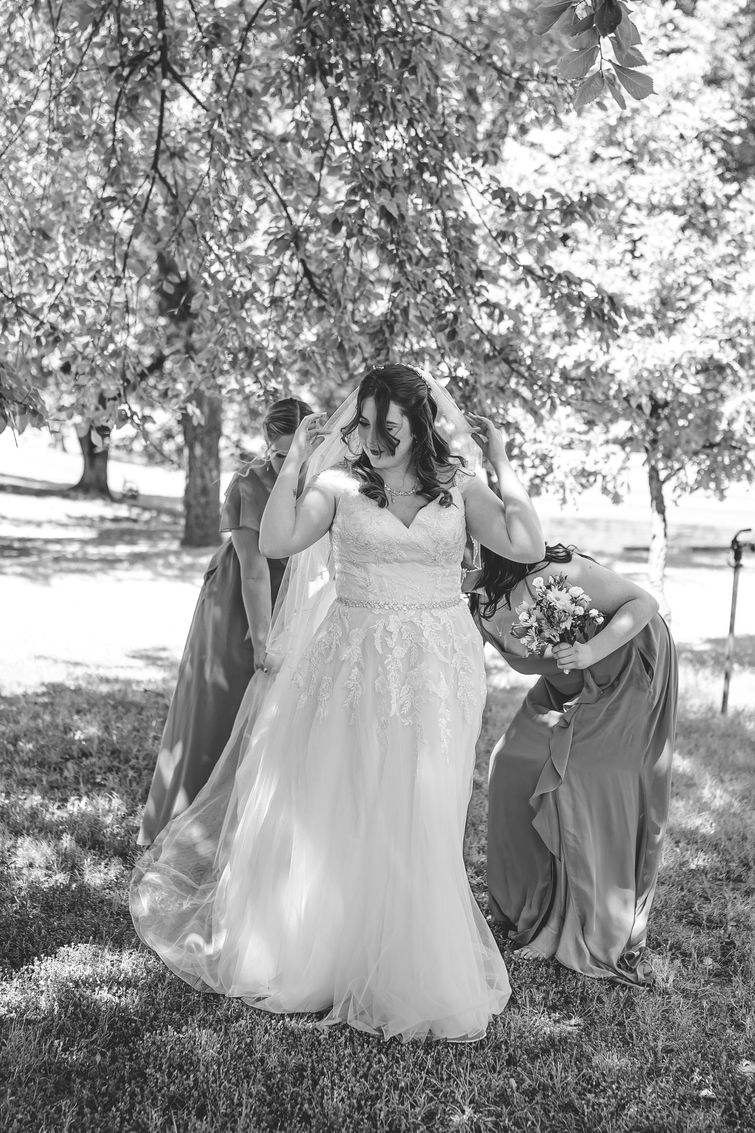 Black and white portrait of bride in lace gown with bridesmaids in flowing dresses.
