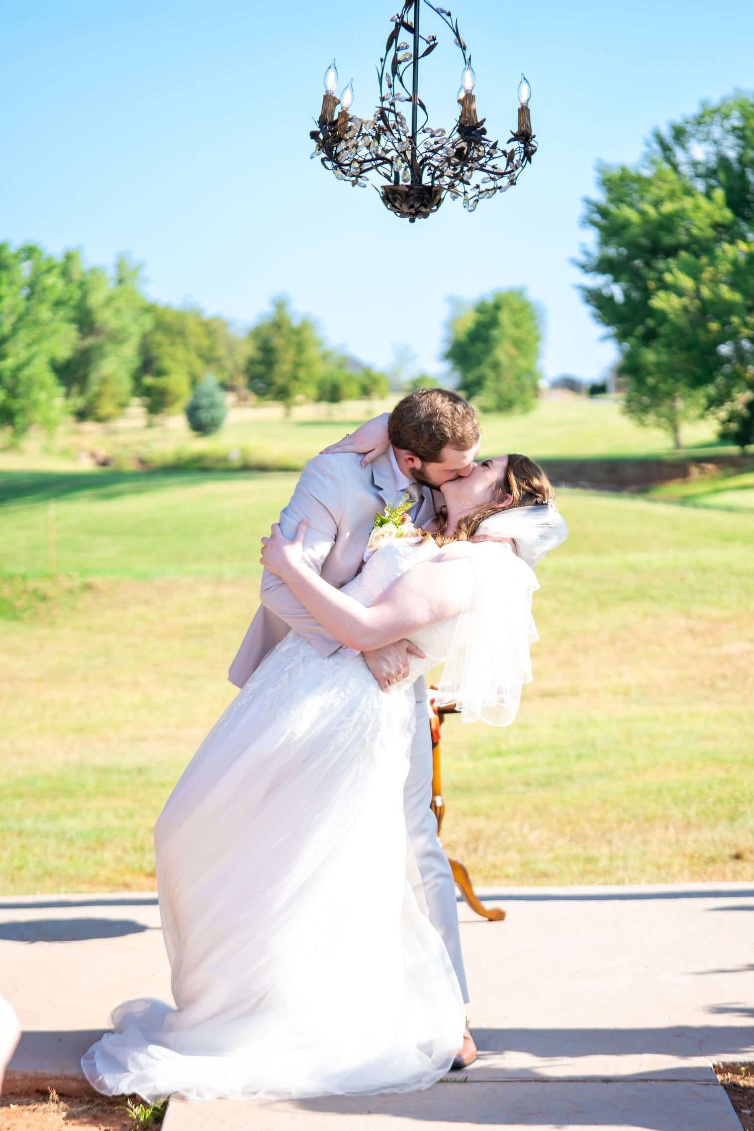 Romantic dip pose under vintage chandelier during outdoor summer wedding.