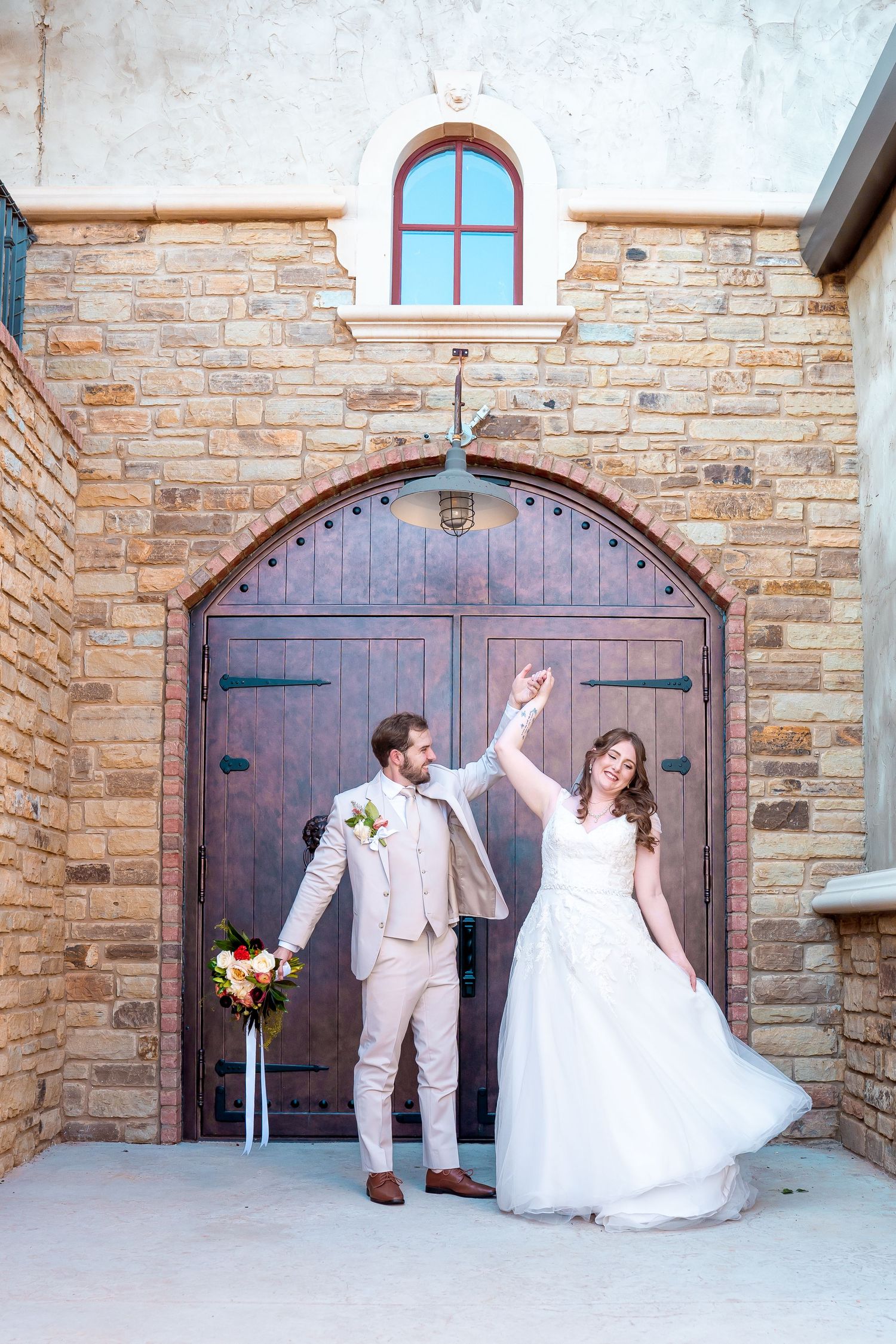 Wedding couple dances in front of a rustic stone church entrance with wooden double doors.