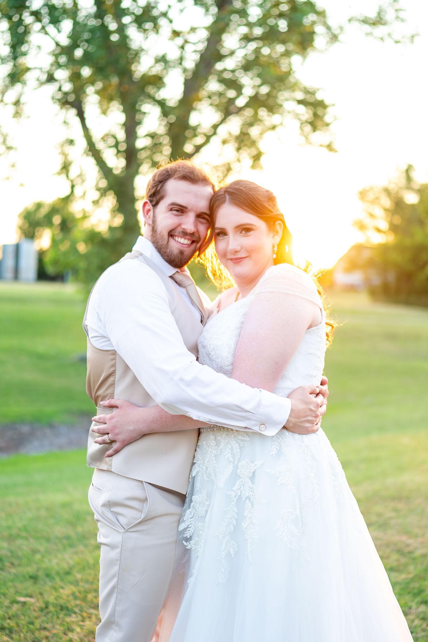 Newlyweds share an intimate moment at sunset in a grassy outdoor setting.