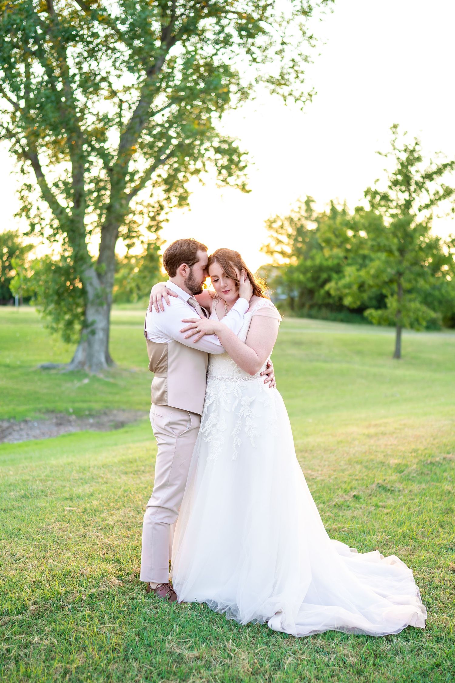 Romantic couple embraces on their wedding day in a sun-drenched garden setting.