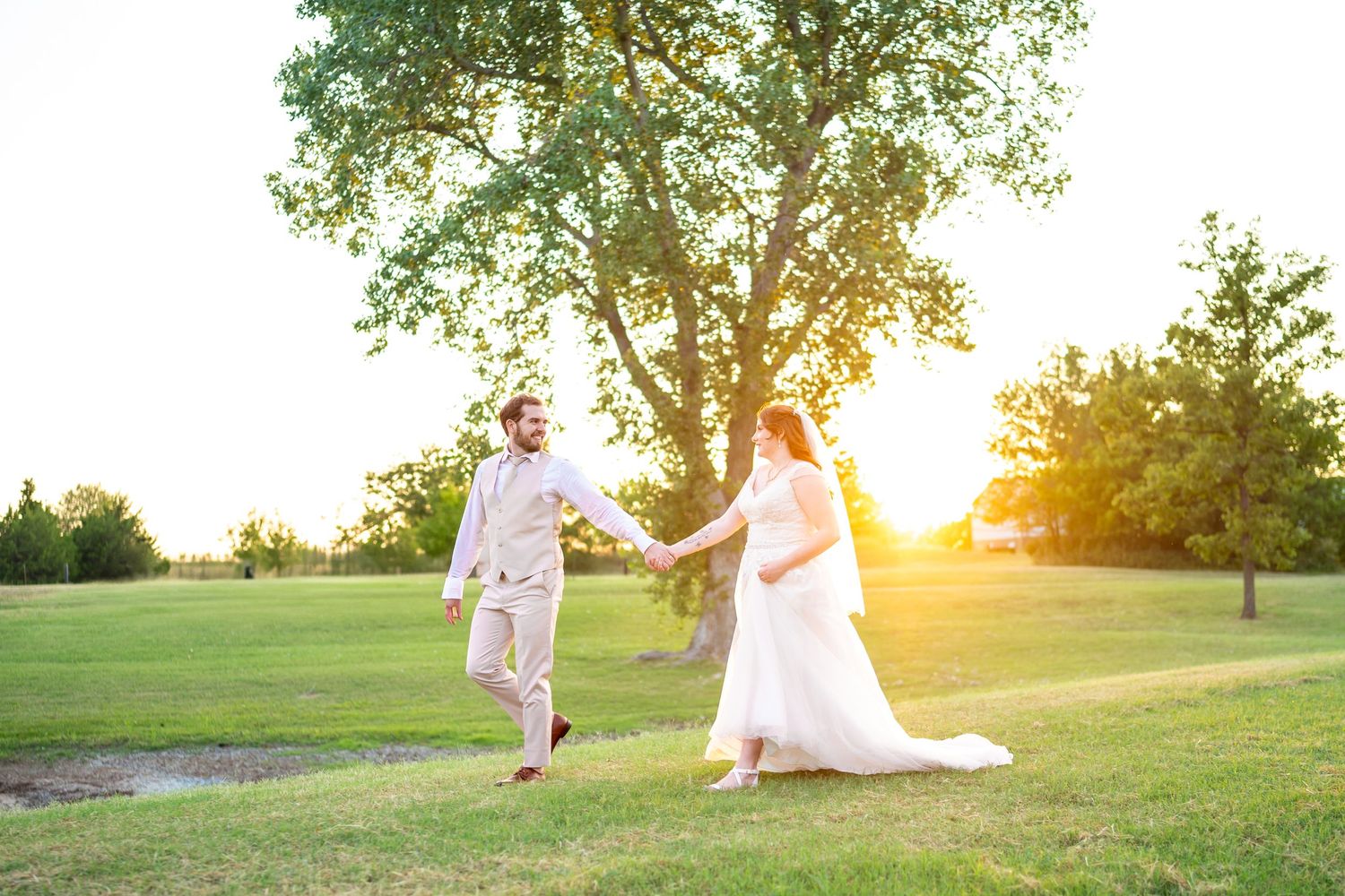 Wedding couple dances playfully in a sunlit field during golden hour.