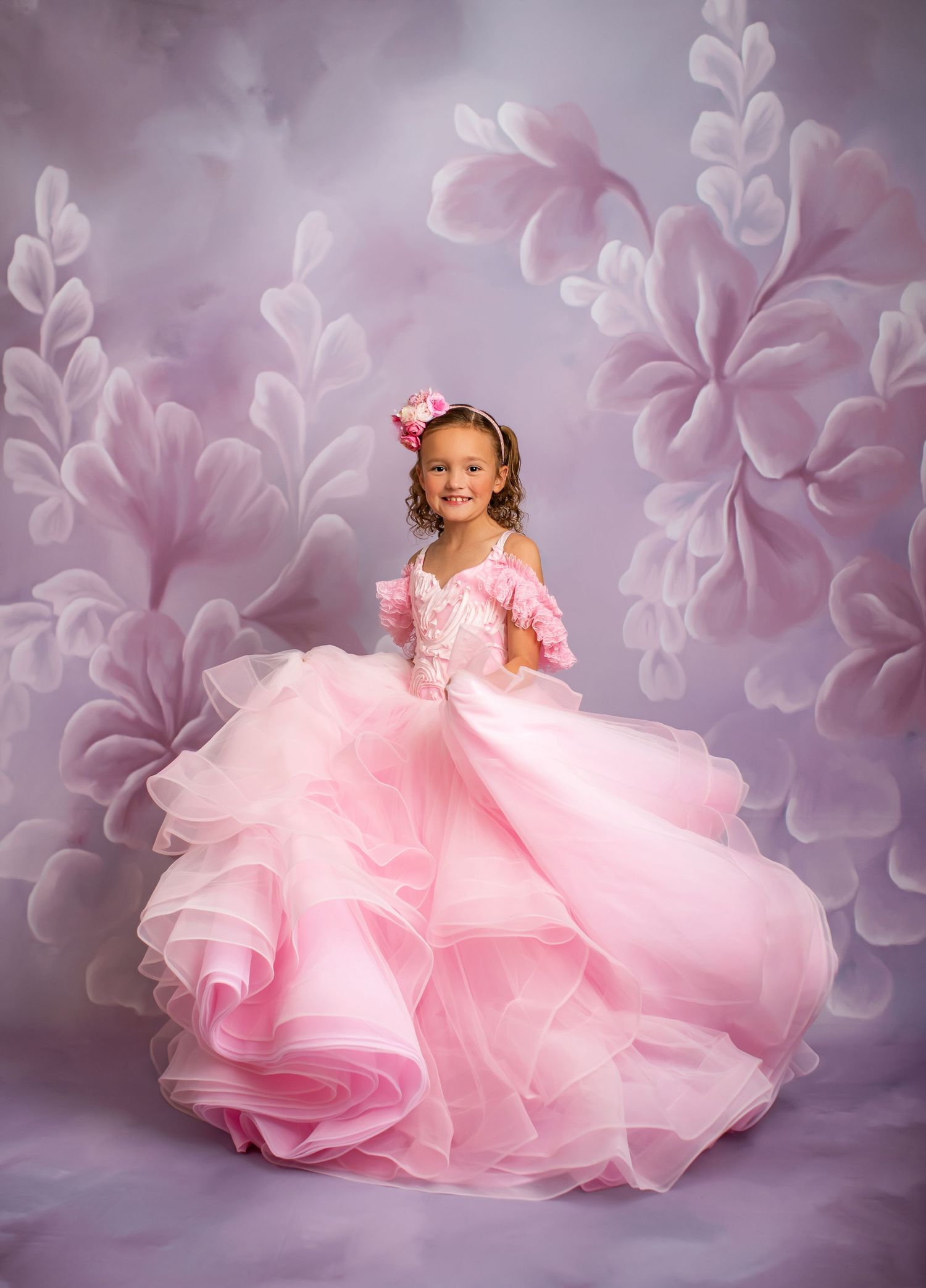 Young dancer twirls in elaborate pink ruffled ball gown against floral backdrop.